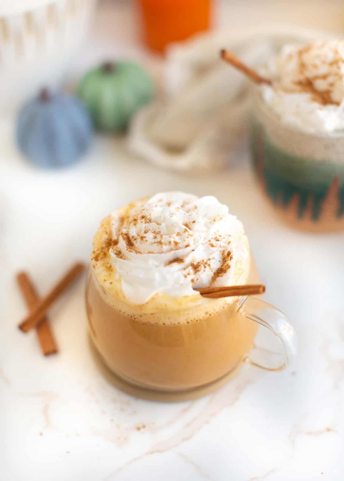 Glass mug of vegan pumpkin spice latte, topped with dairy free whipped cream.