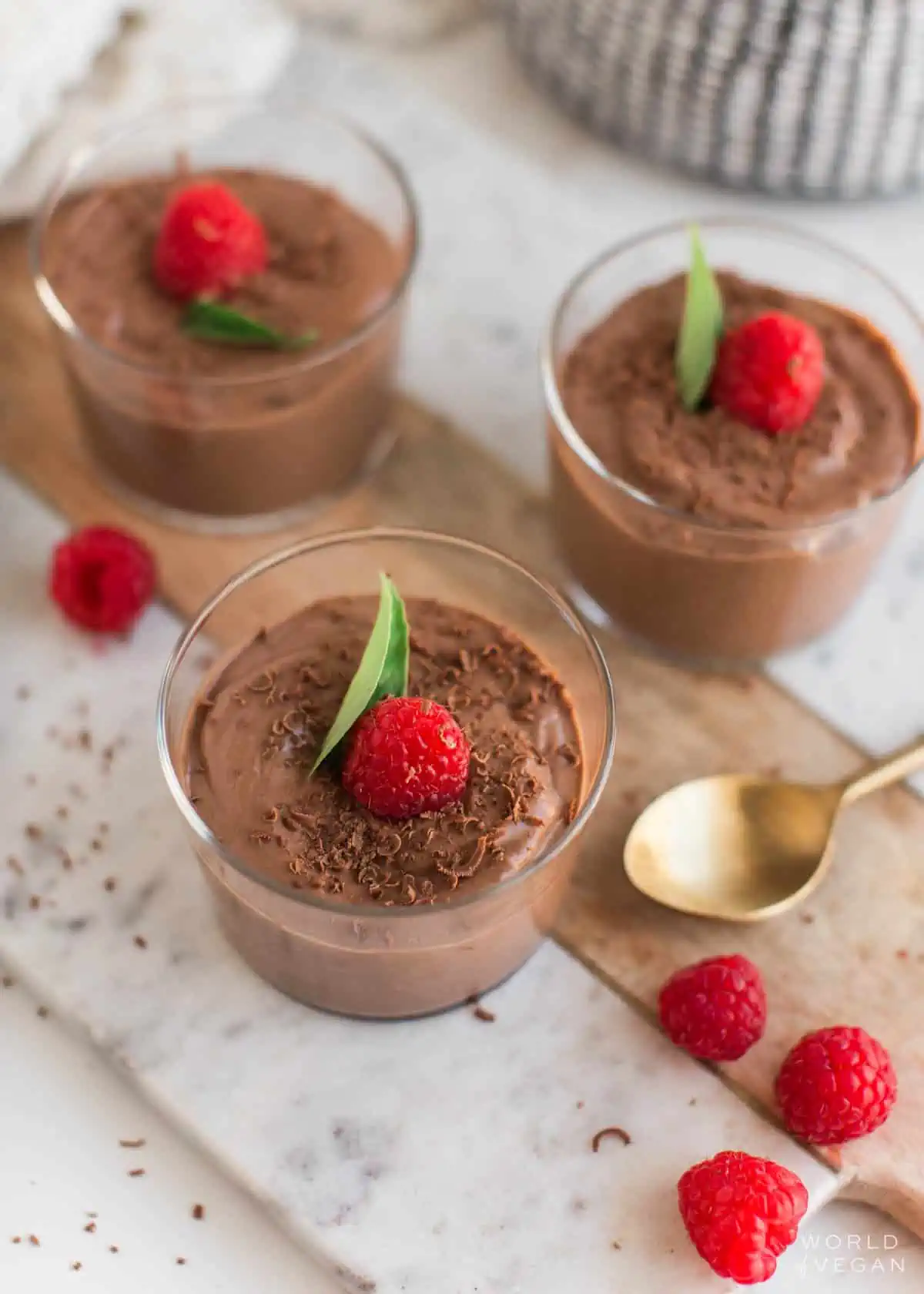 Small glass bowls of silken tofu chocolate mousse with raspberries scattered around.