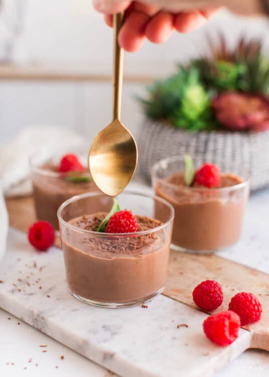 A hand holding a spoon over a jar of silken tofu mousse.