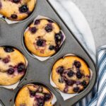 Vegan blueberry muffins in baking tin with golden-domed tops.