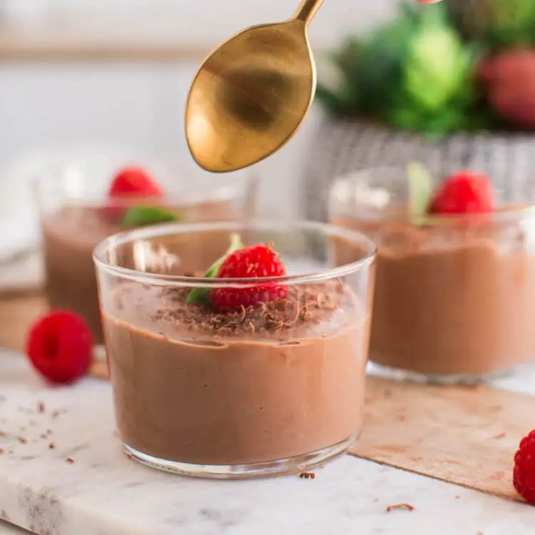 Vegan chocolate mousse in glass jars topped with chocolate shavings and fresh raspberries.