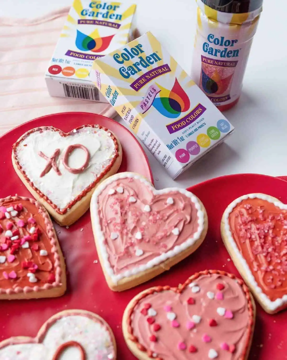 Two boxes of Color Garden dyes next to an assortment of heart-shaped Valentine cookies on a red, heart-shaped plate.