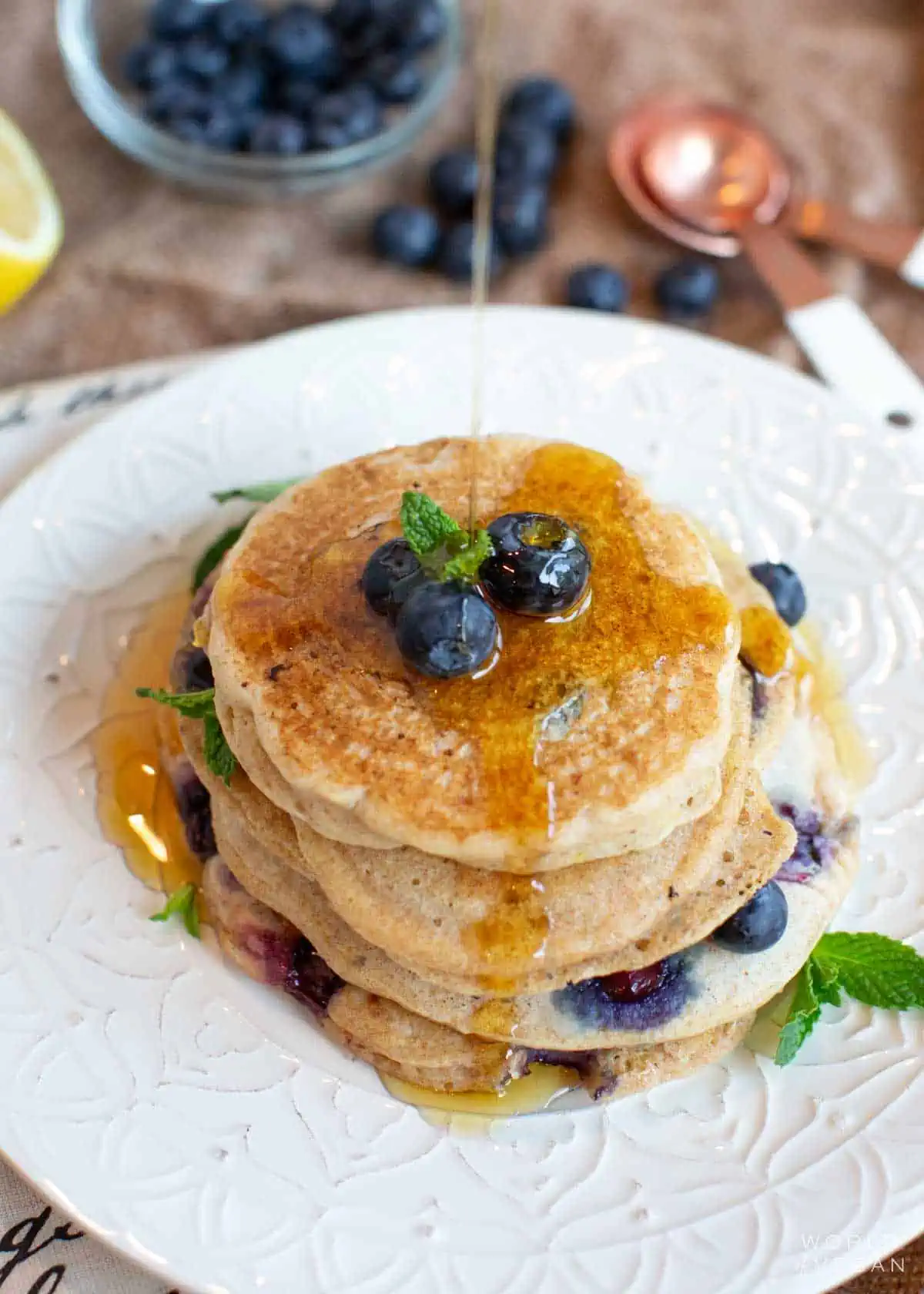 Overhead view of a stack of blueberry vegan pancakes, topped with more blueberries and maple syrup.