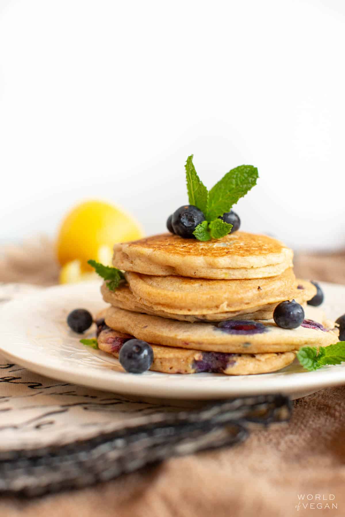 A small stack of vegan blueberry pancakes on a plate, topped with fresh blueberries.