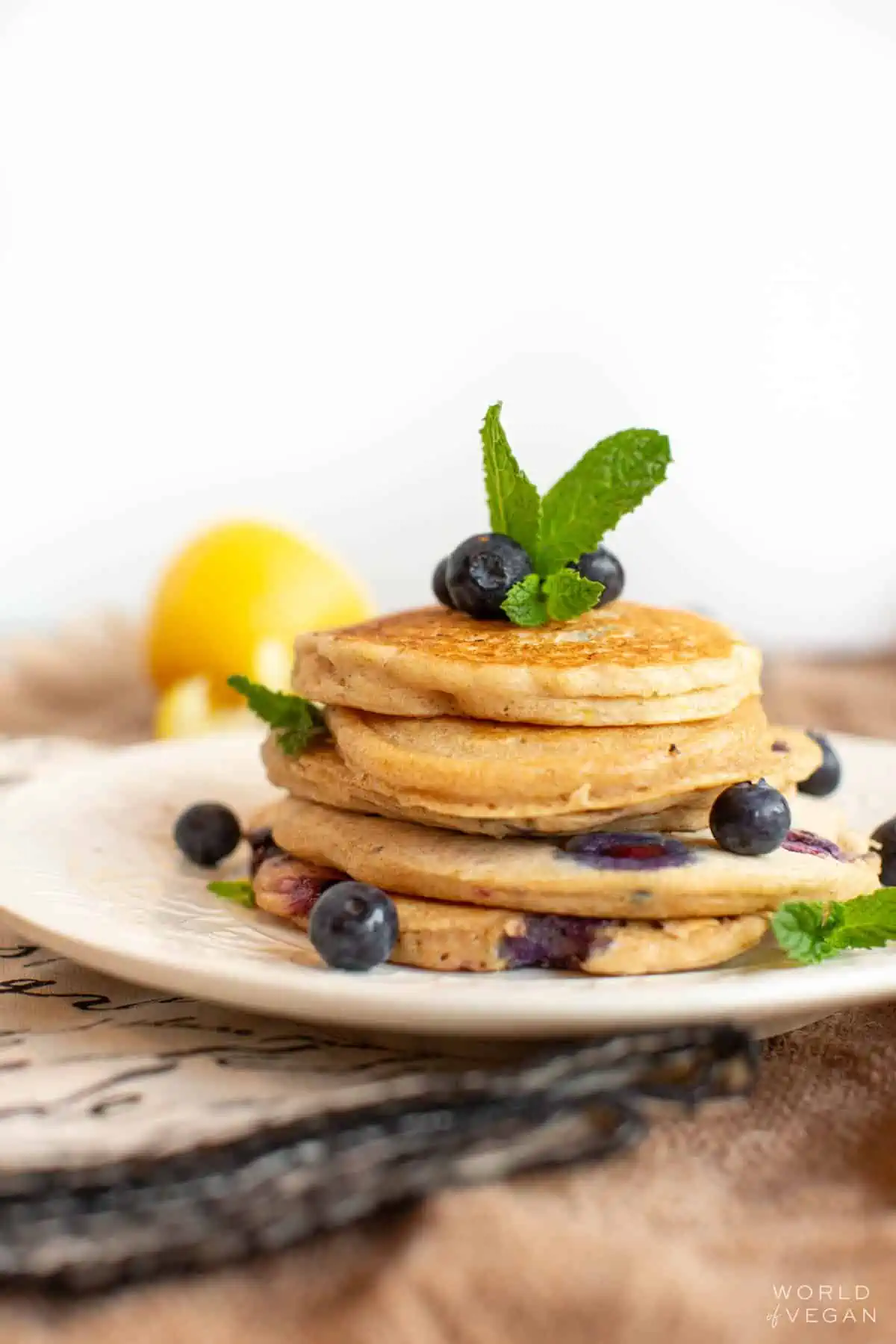 A small stack of vegan blueberry pancakes on a plate, topped with fresh blueberries.