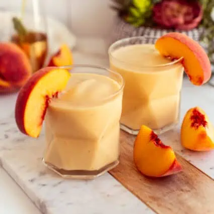 Two small glasses of banana peach smoothie topped with peach slices.