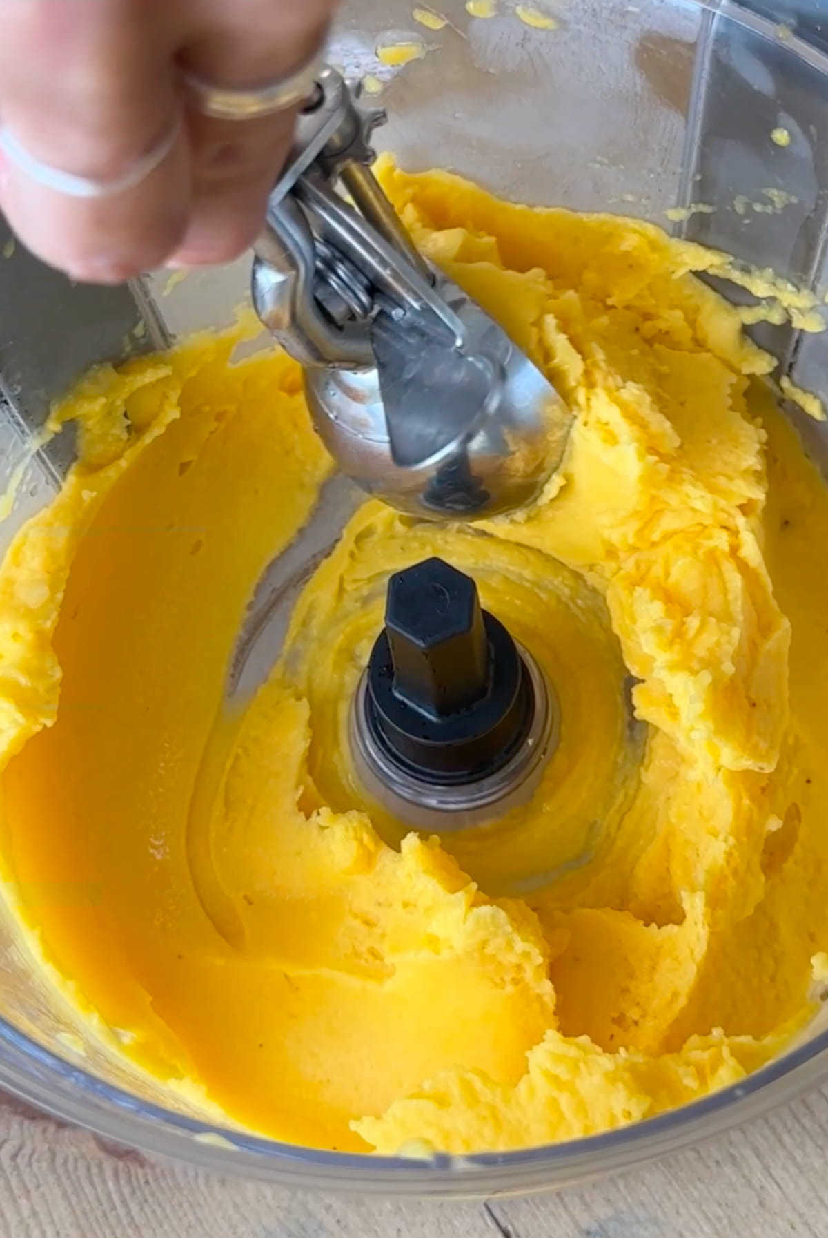 Blended mango sorbet in a food processor with a hand using an ice cream scoop to scoop some out.