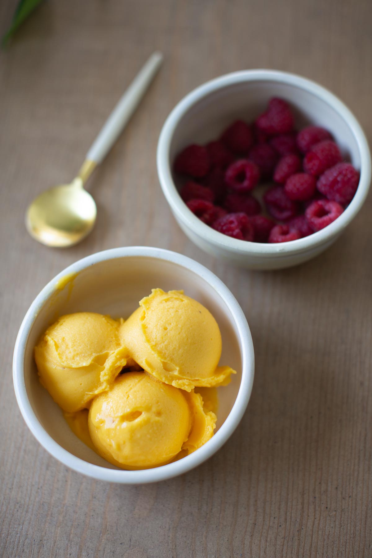 A bowl of mango sorbet and raspberries on a table.