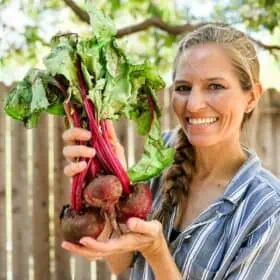 A woman holding out a bundle of fresh raw red beets with their greens.