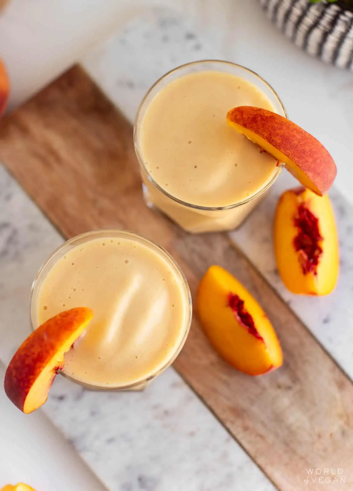 Overhead view of two glasses of peach banana smoothie, serve with fresh peach slices.