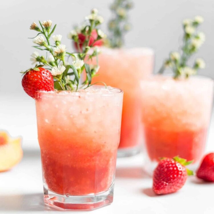 Glass of strawberry peach spritzer with ice, garnished with fresh strawberries.