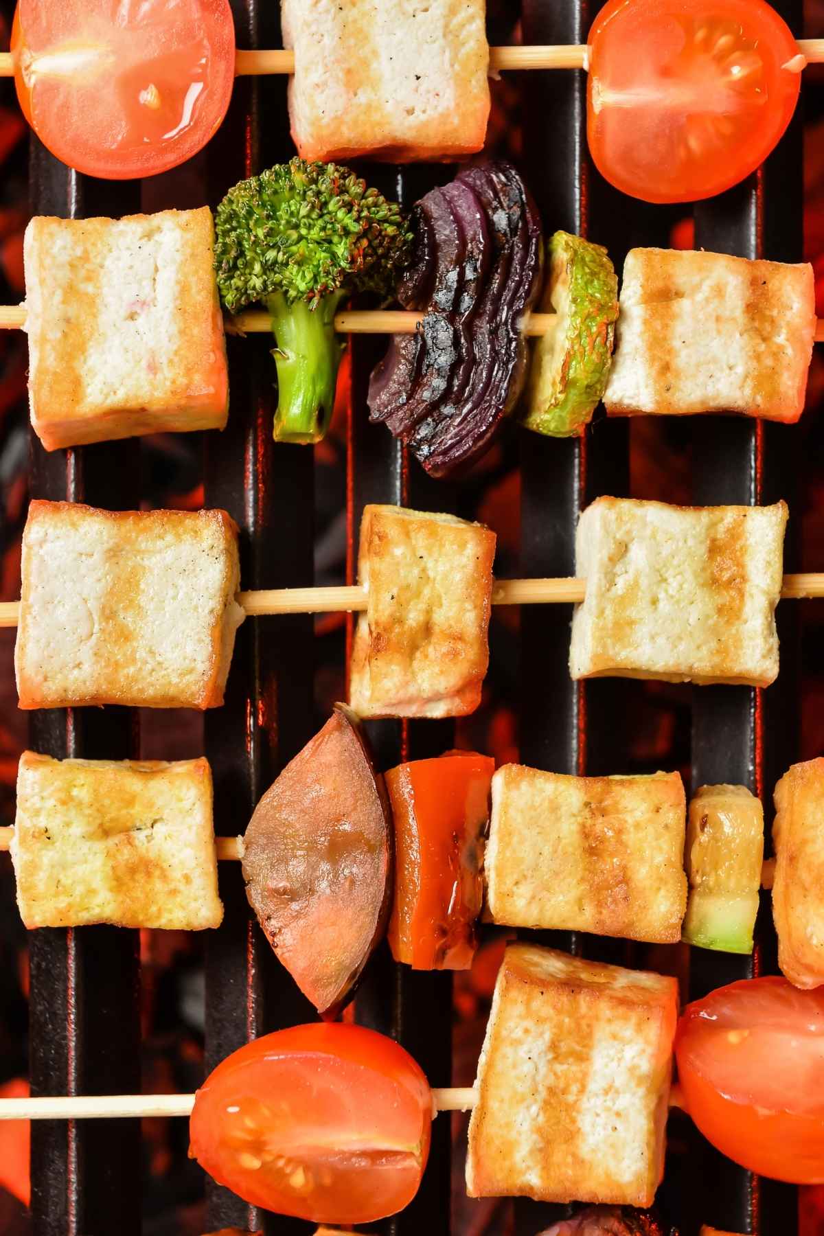 Tofu with colorful vegetables over a grill flame.
