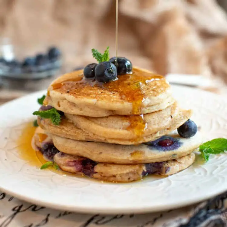 Vegan blueberry pancake stack, with maple syrup pouring over the top.
