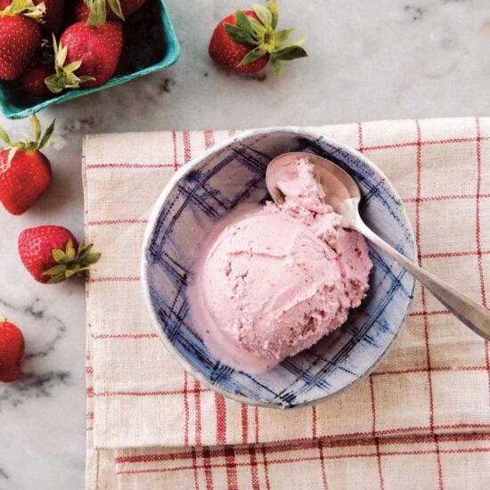 A bowl of vegan strawberry ice cream with fresh strawberries on a marble countertop.