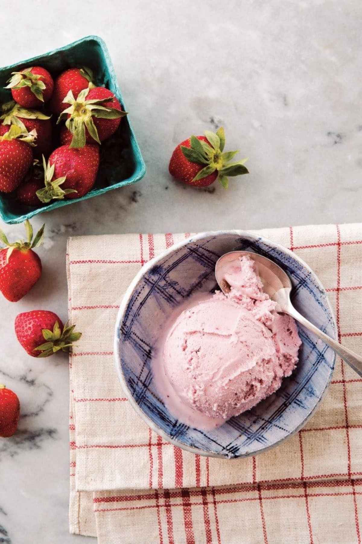 A creamy scoop of dairy-free strawberry ice cream in a blue ceramic bowl with fresh strawberries.