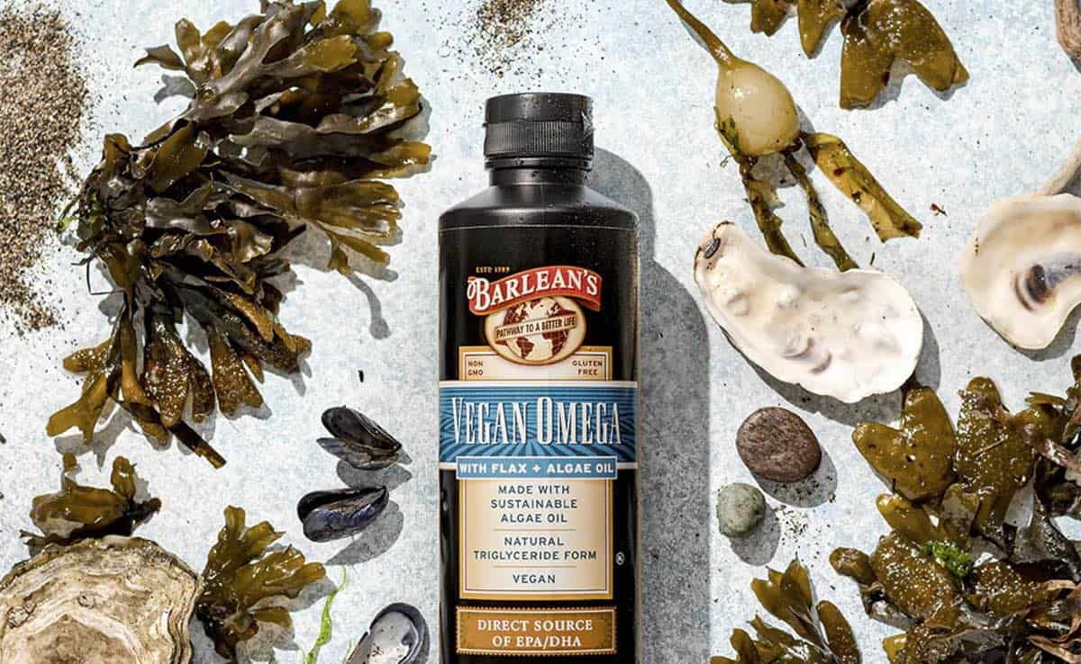 A bottle of Vegan omega-3 vitamin oil from Barlean's on a flat table surrounded by fresh sea kelp.