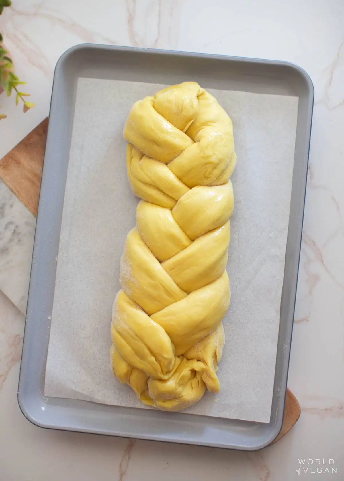 Three-strand braided vegan challah bread on a baking tray.