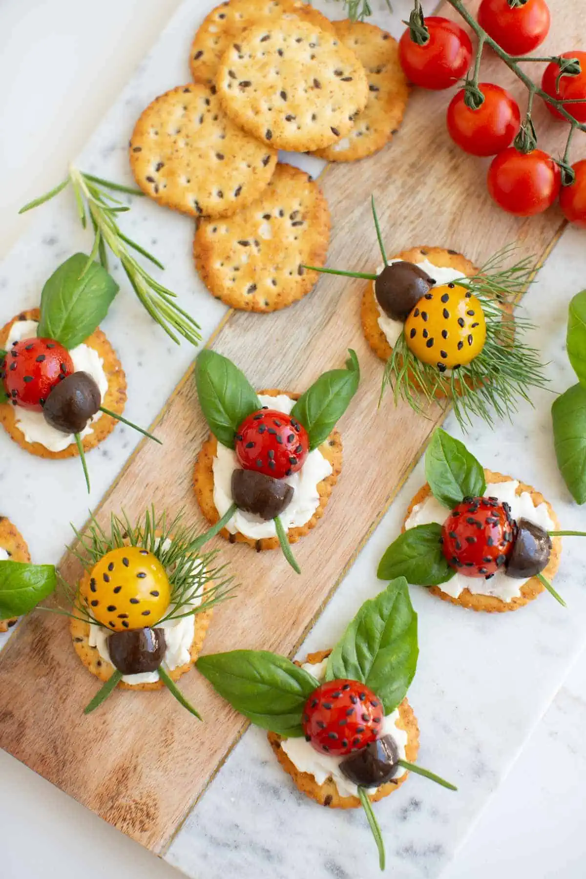 Crackers topped with cream cheese, cherry tomatoes, black olives, basil, and chives to look like ladybugs.