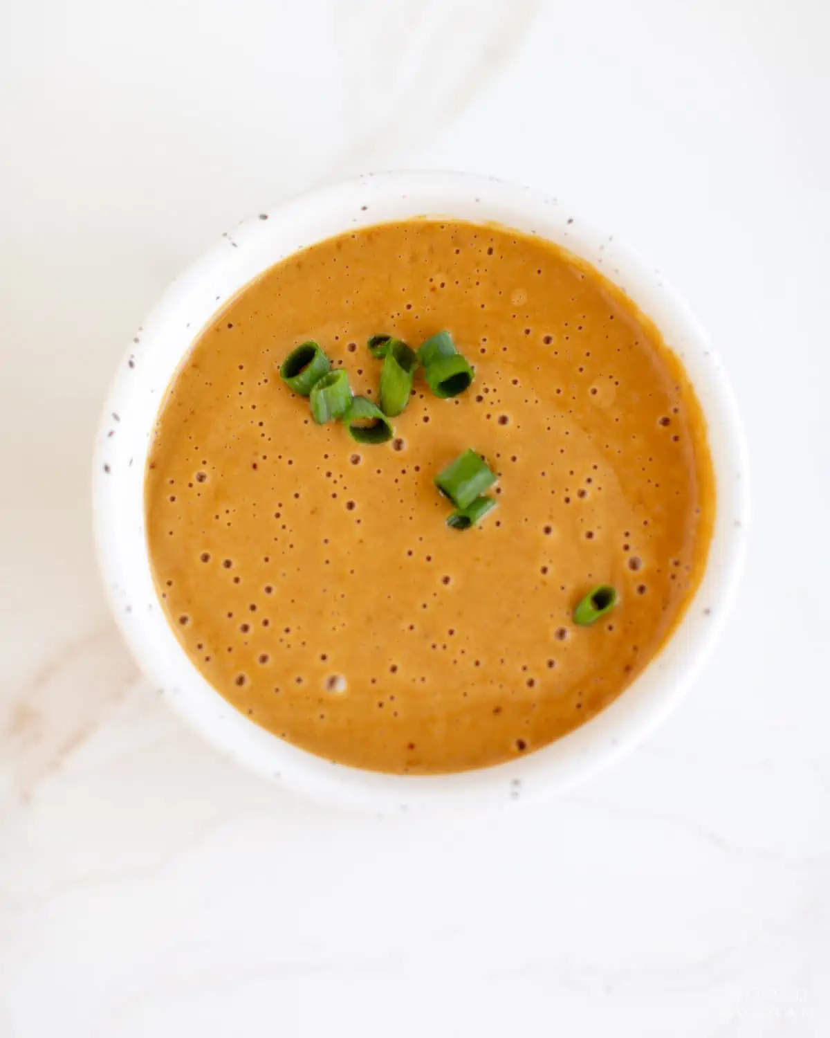 Peanut sauce for the cold noodle salad in a small bowl, garnished with sliced green onion.