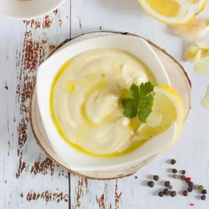 Small bowl of vegan aioli garnished with fresh parsley and a slice of lemon.