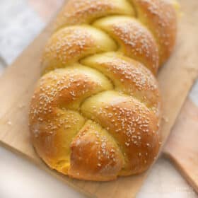 Braided vegan challah bread on a cutting board, topped with sesame seeds.