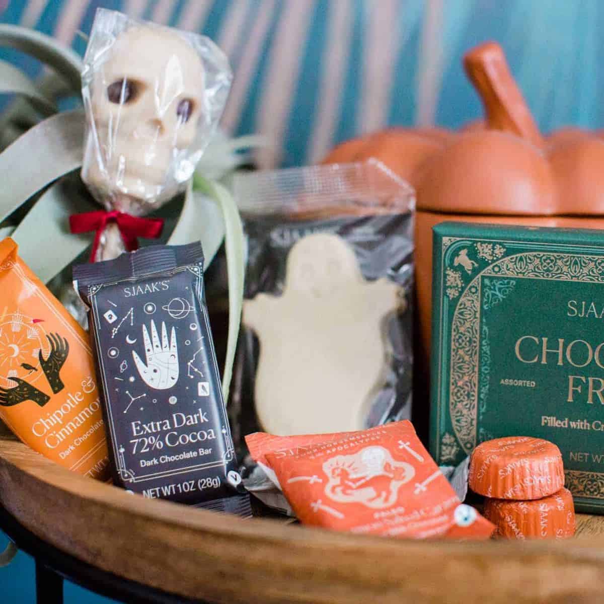 A bunch of vegan halloween candy and Sjaaks chocolate on a table with a pumpkin and skeleton and ghost and other fall decor.