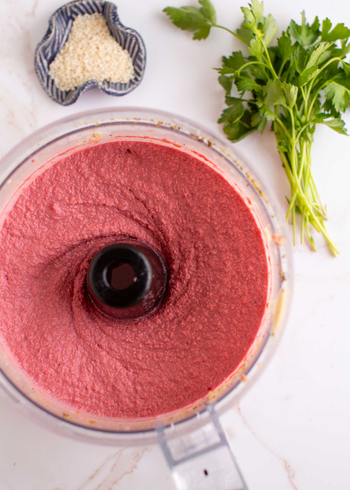 Blended pink hummus in a food processor on a countertop. 