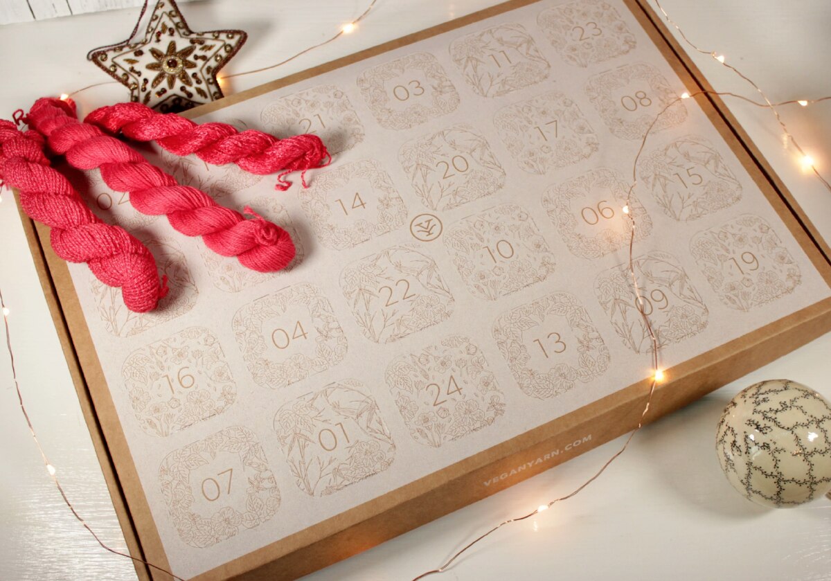 A craft box decorated and cut with advent day boxes accessorized with red skeins of yarn and fairy lights.