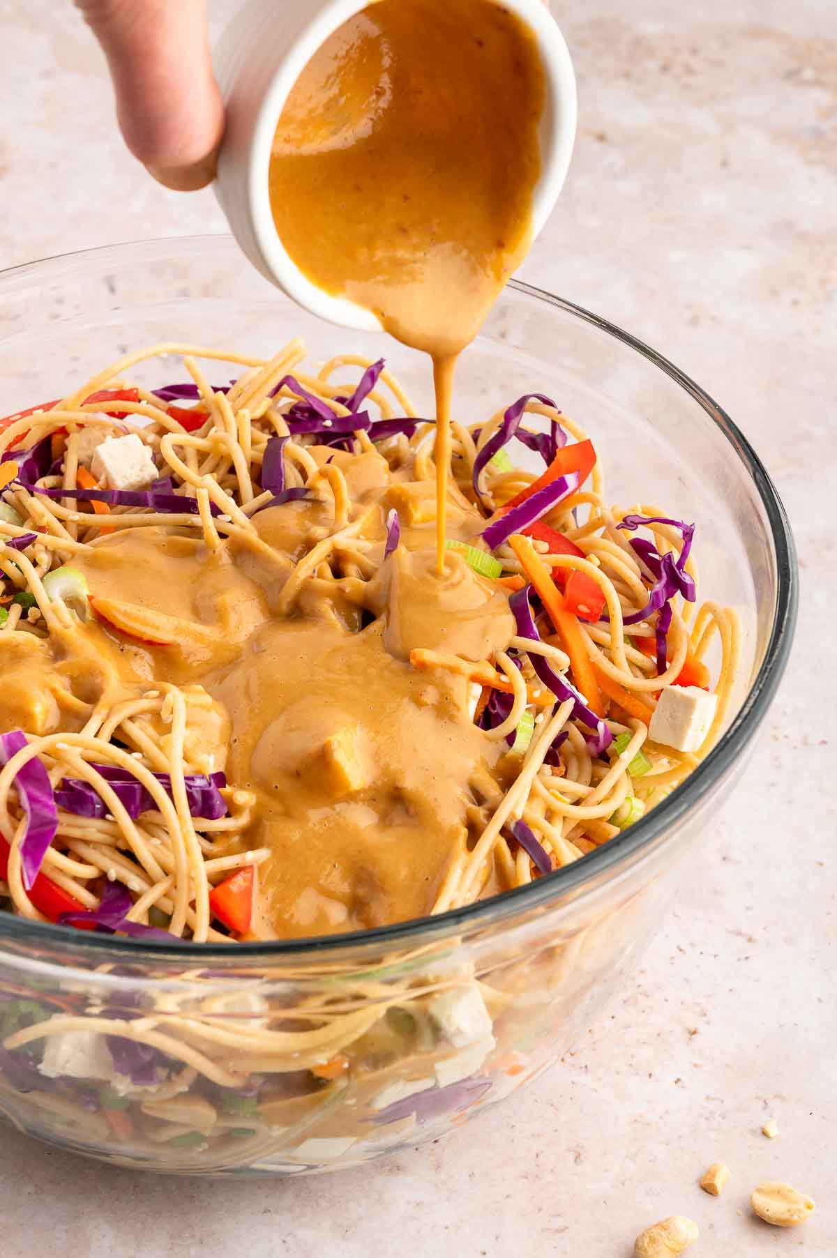 A hand pouring peanut sauce over a cold noodle salad.