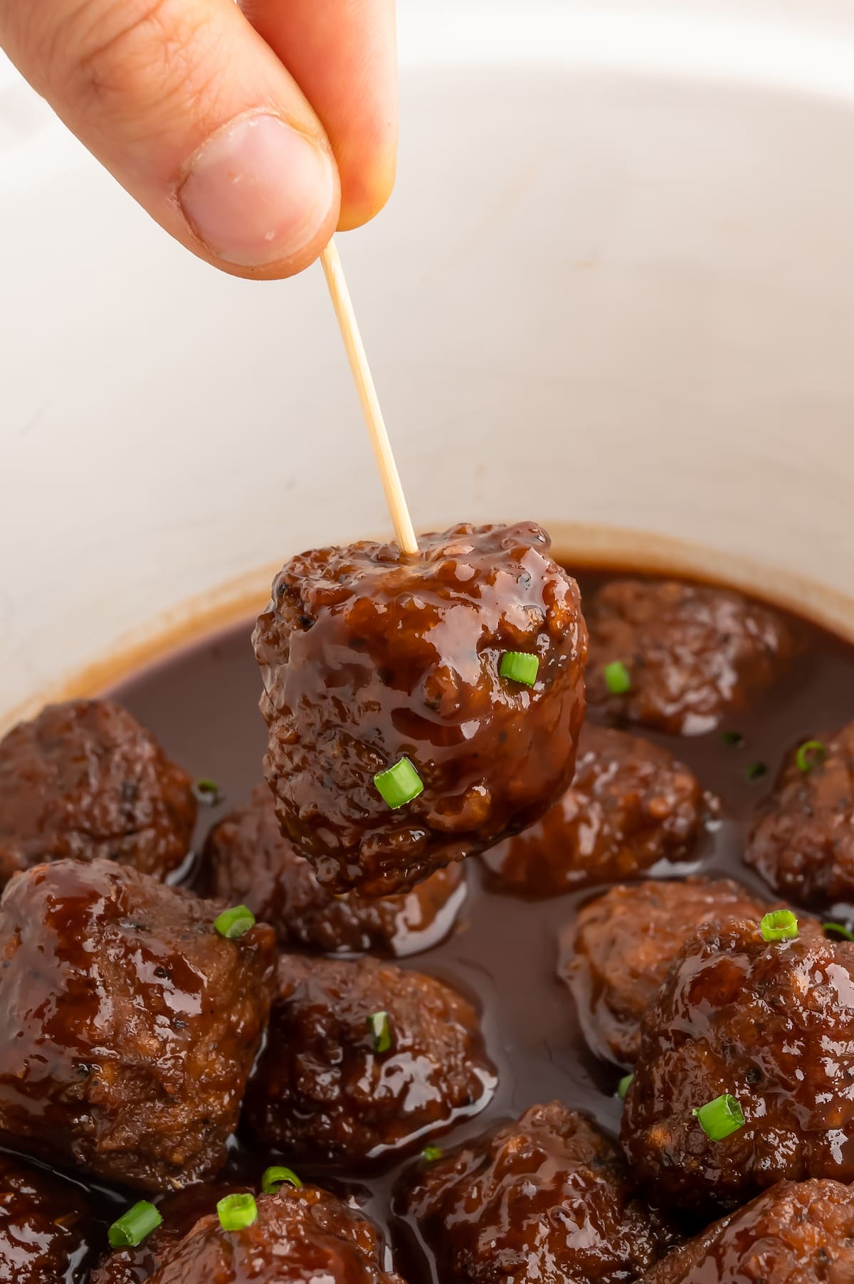 A hand using a toothpick to pick up one of the vegan bbq sauce meatballs.