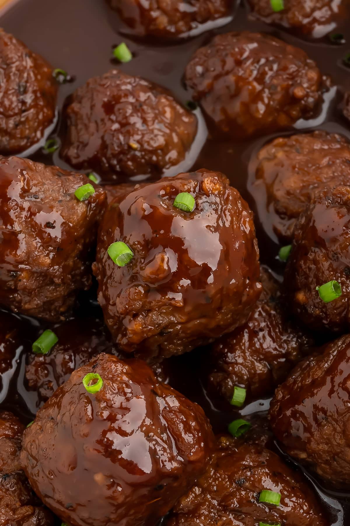 Vegan bbq sauce meatballs in a slow cooker topped with chopped chives.