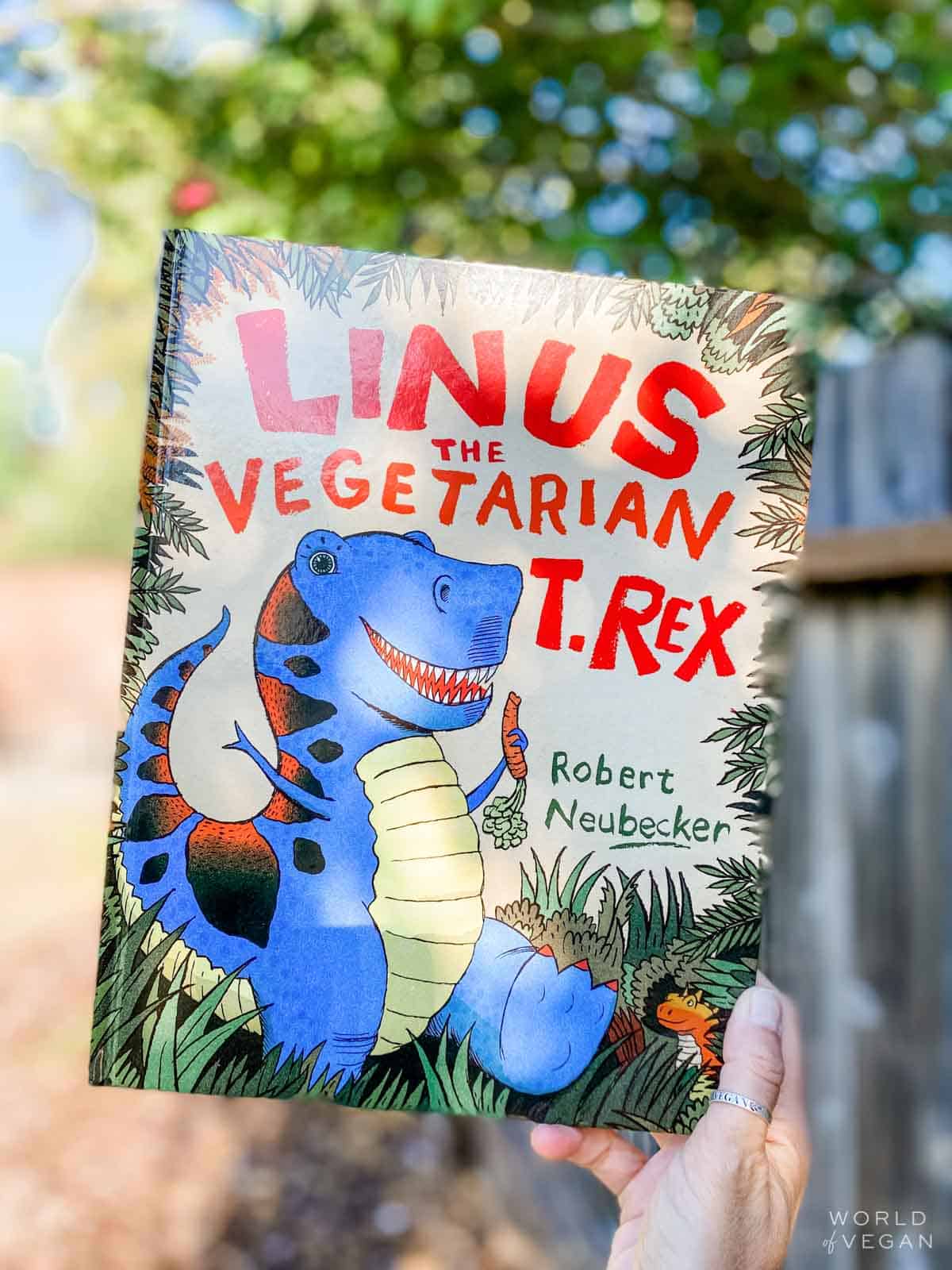 Holding up the vegan children's book called Linus the Vegetarian T-Rex.