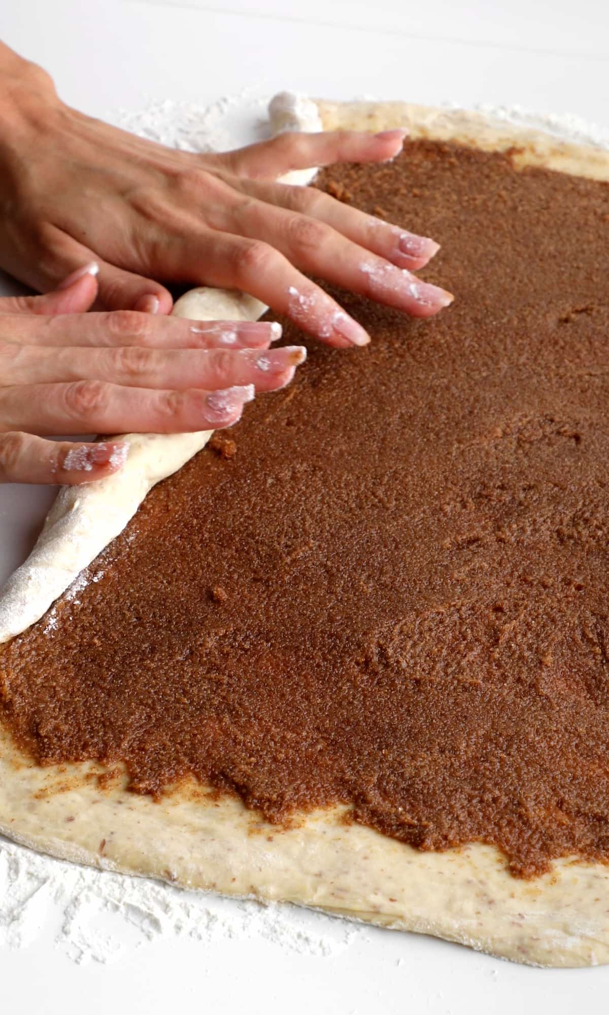 Hands rolling up the cinnamon roll starting on the long end.