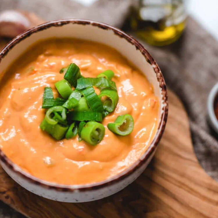 A serving bowl filled with vegan buffalo chicken dip and topped with sliced green onions.