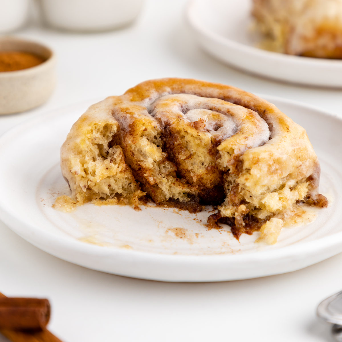 A vegan cinnamon roll on a plate with a few bites missing to show the inside.