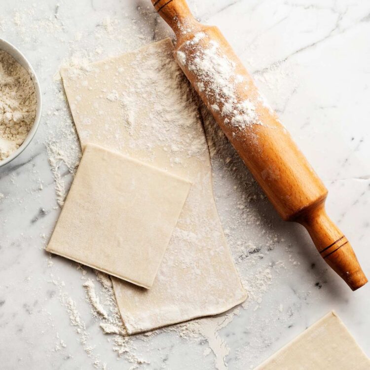 Vegan puff pastry rolled out on a floured surface next to a rolling pin.