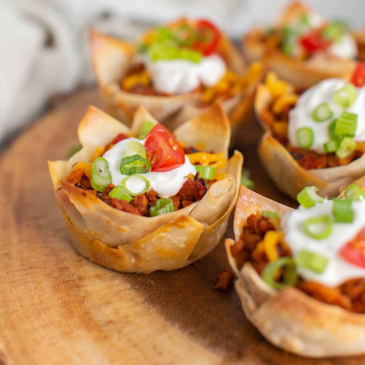 Vegan taco cups topped with vegan sour cream and green onions, served on a wooden platter.
