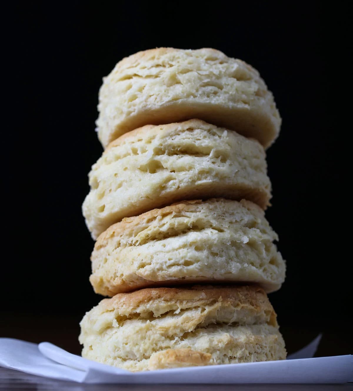 Stack of four tall, golden vegan biscuits with flaky layers against a dark background.