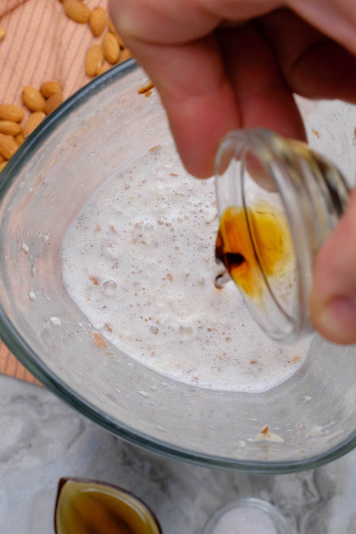 Vanilla being added to almond milk in a blender.