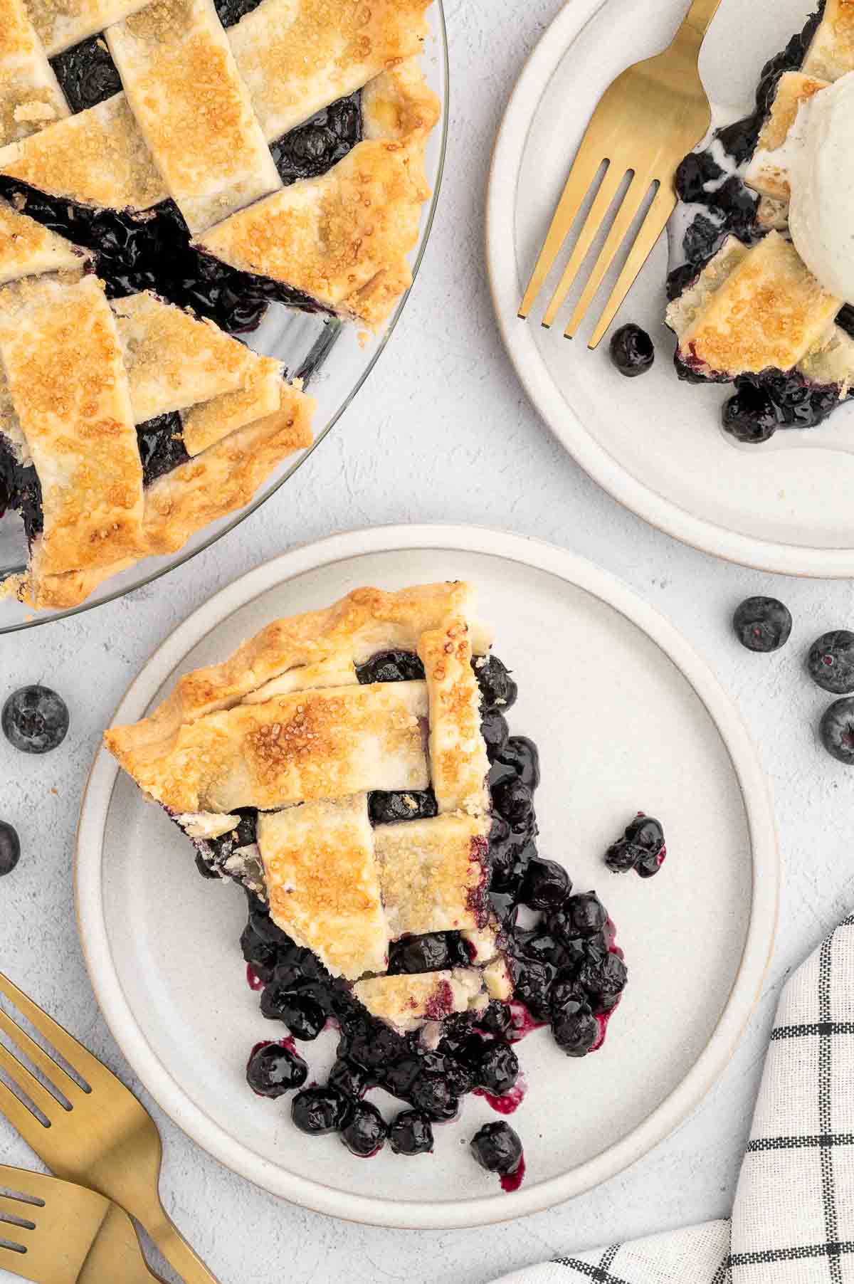 A slice of vegan blueberry pie with a lattice pattern golden crust on top, sitting on a plate.