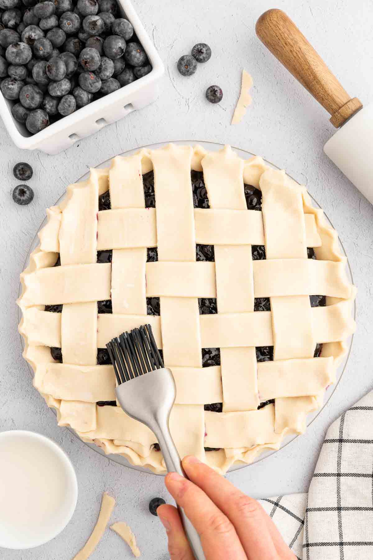 A hand using a basting brush to add a light layer of soy milk on top of the crust.