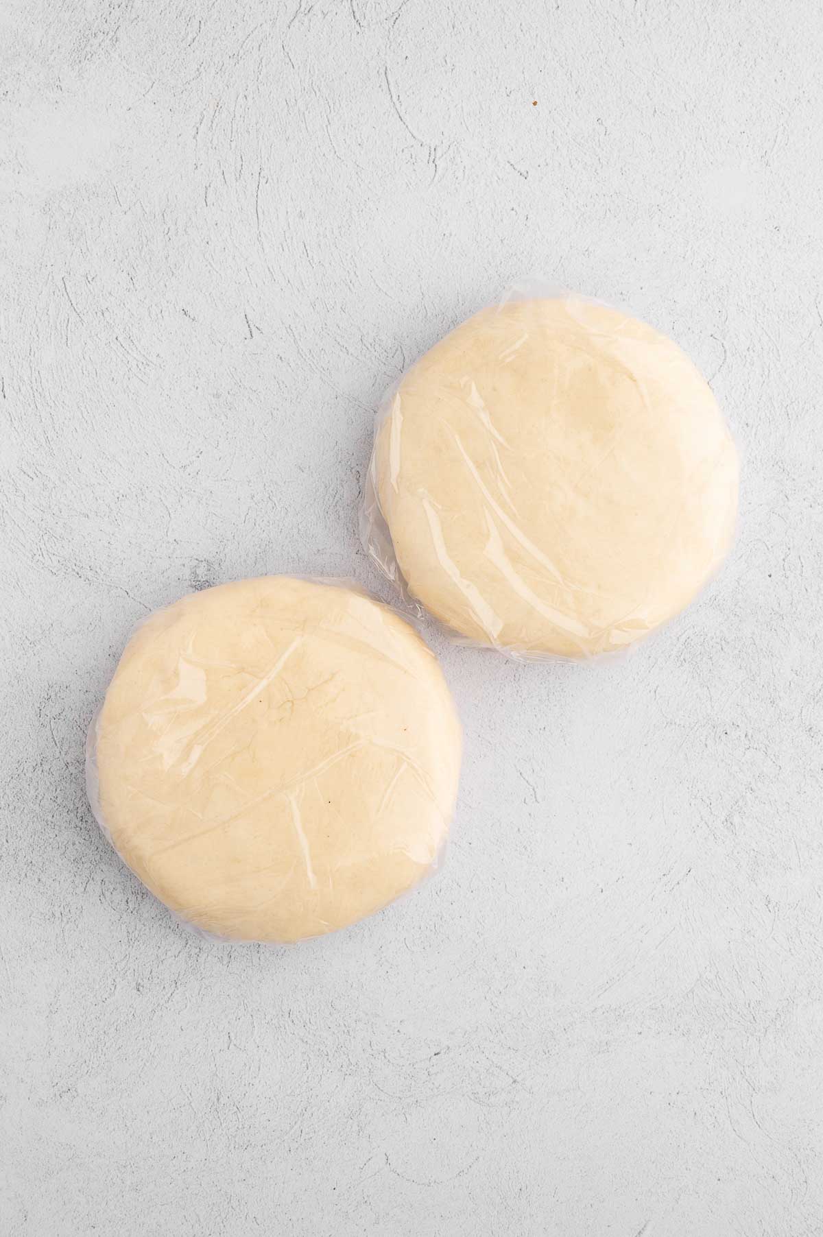 Each half of the vegan pie crust dough rolled and flattened into discs, then wrapped with plastic wrap.