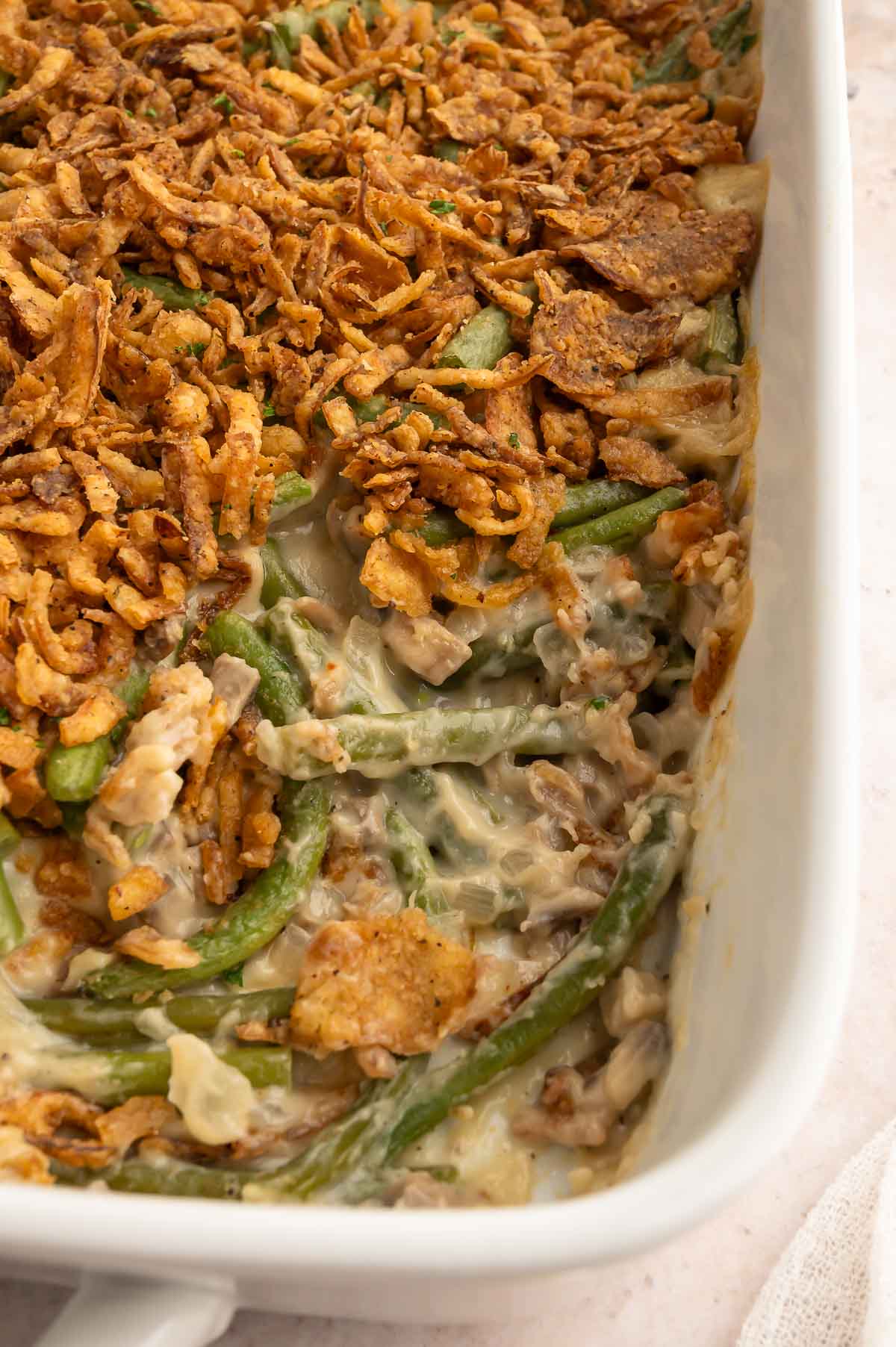 A large casserole dish of vegan green bean casserole with some of the crispy onions removed from the top to show the creamy beans below.
