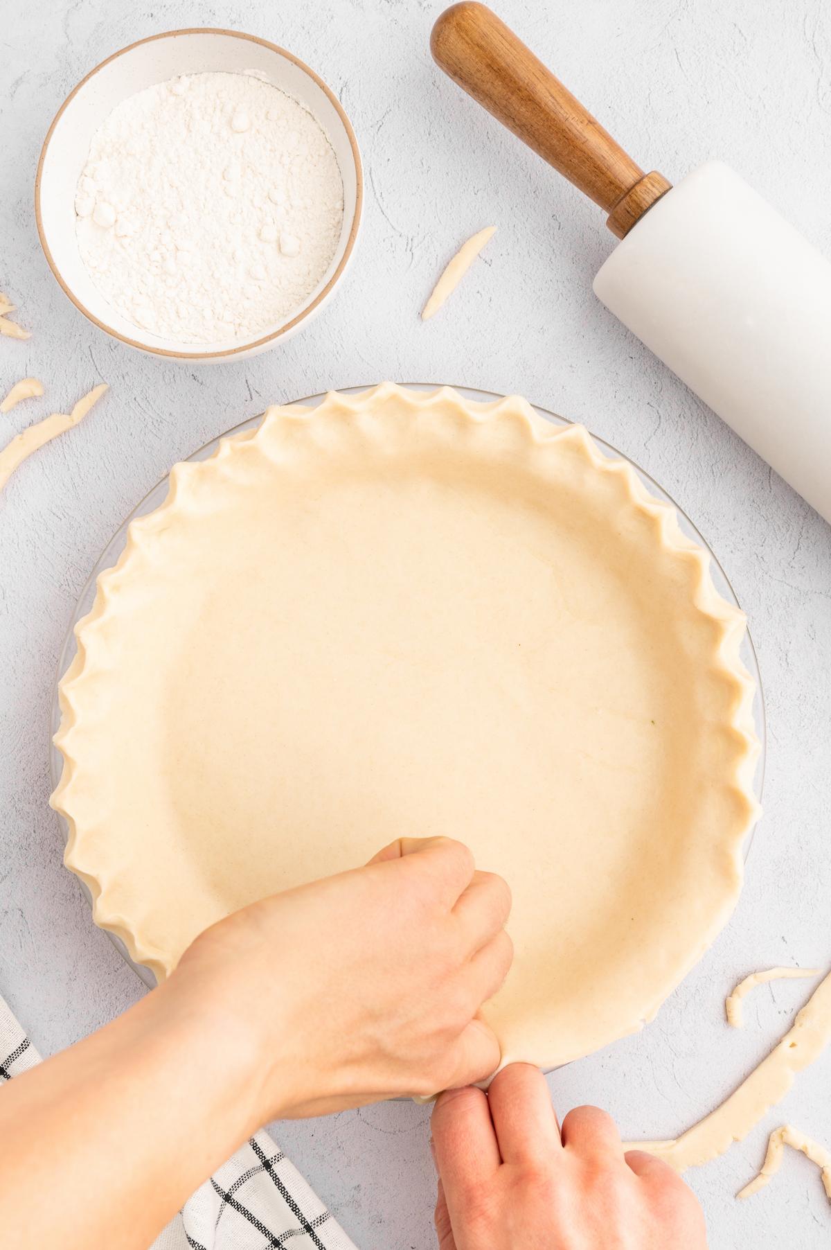 Hands fluting the edge of the pie crust.