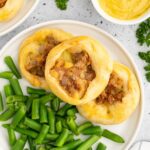 Three knishes on a plate served with green beans and mustard.