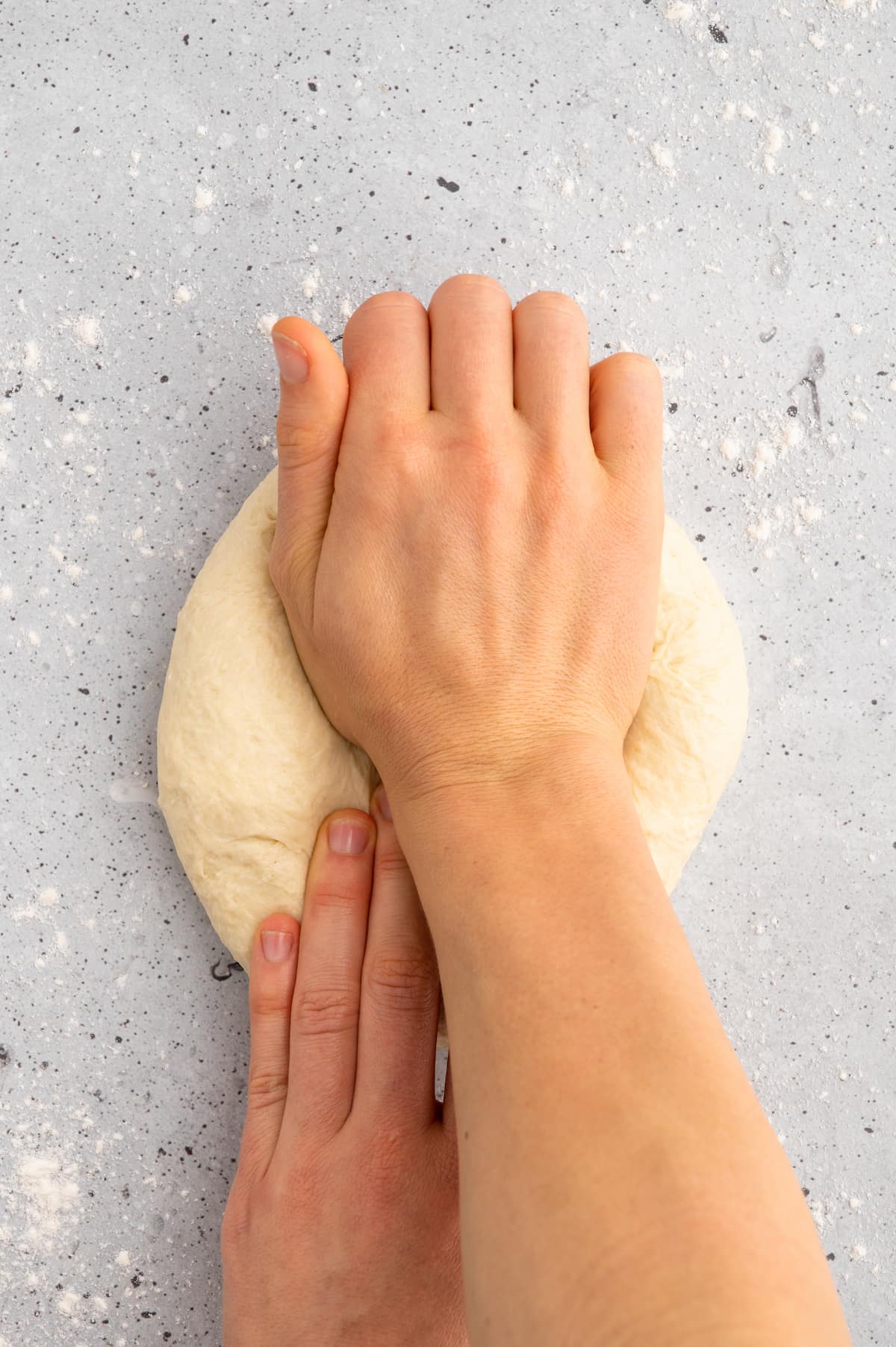 A pair of hands kneading the knish dough on a floured surface.
