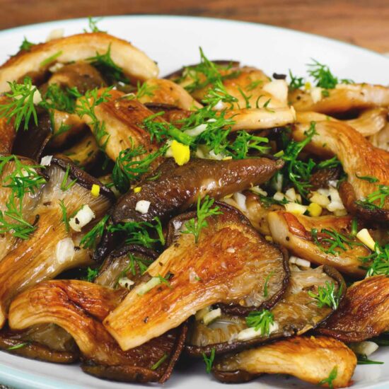 A plate of golden oyster mushrooms topped with fresh herbs and minced garlic.