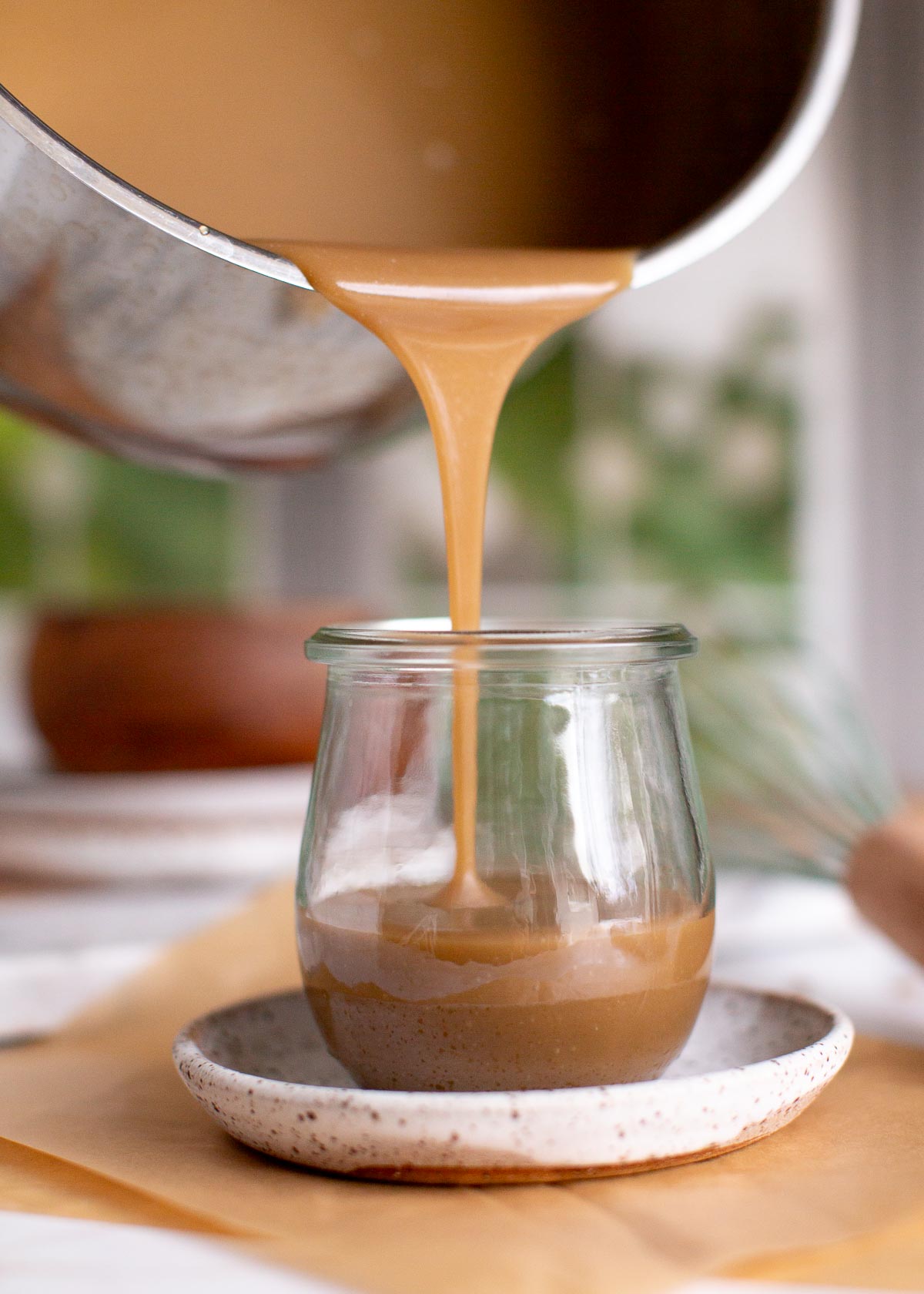 Pouring vegan caramel from a pot into a glass jar.