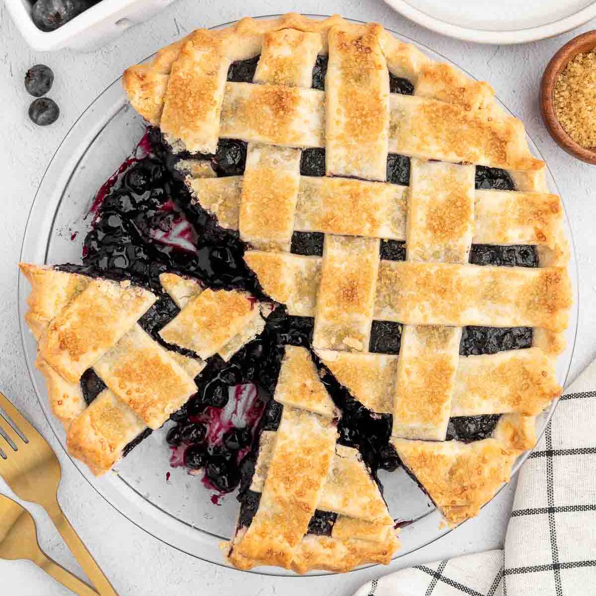 A vegan blueberry pie with a cross-hatch pastry crust sliced with blueberry filling pouring out.
