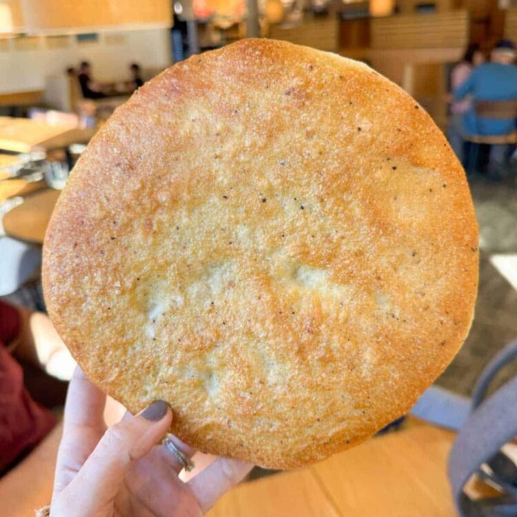 Hand holding up a round piece of golden-brown flatbread in a café setting.